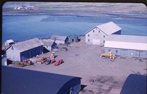 Photo of a group of buildings including a warehouse, a two-story building on the waterfront.